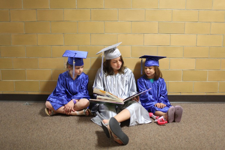 Image: Three students dressed in graduation caps and gowns sit and read a book at the elementary school in Cyrus, Minn.