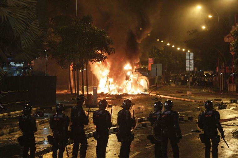 Image: Riot police stand guard near a burning vehicle on Dec. 8, 2013