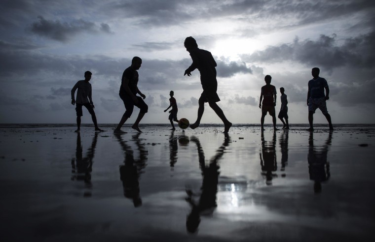 Image: People are silhouetted as they play football at a beach along the Arabian Sea in Mumbai