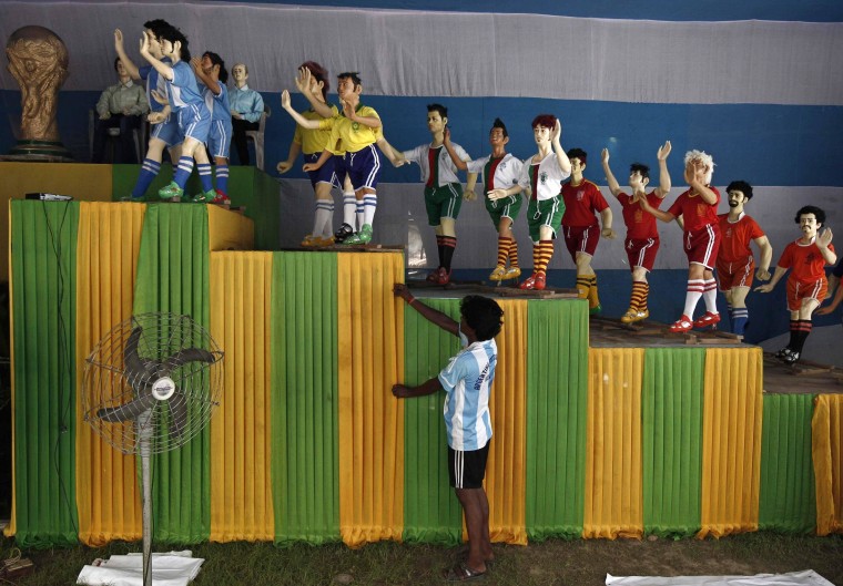 Image: An Indian soccer fan of Argentina adjusts a cloth in front of clay models of soccer players inside a "Pandal" in Kolkata