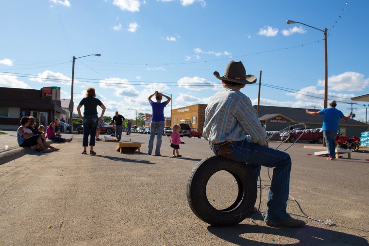 Image: A young boy takes a break from roping straw bale "calves" to watch people toss bean bags during a summer block party on Main Street in Circle, Mont.