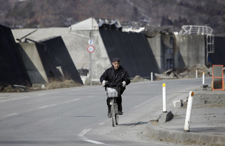 A man pedals his bicycle by a heavily damaged breakwater that is awaiting reconstruction in Otsuchi in northeastern Japan on March 4, 2014.