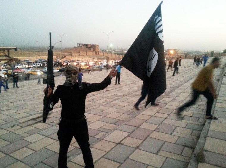 Image: A fighter of the ISIS holds a flag and a weapon on a street in Mosul