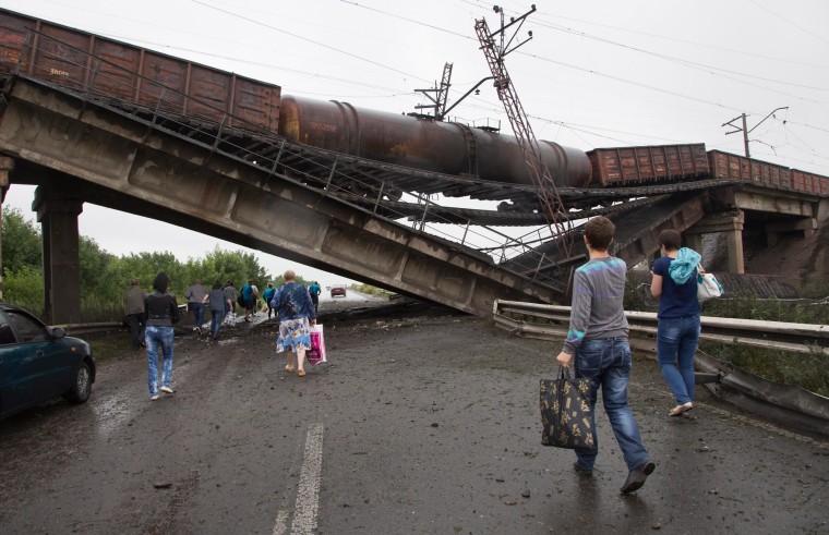 Image: People walk under a destroyed railroad bridge over a main road leading into the east Ukraine city of Donetsk