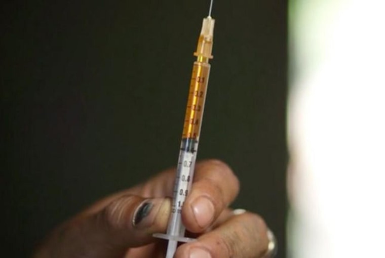Image: An addict holds a syringe filled with orange-colored heroin mixed with saline.