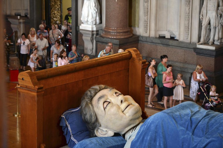Image: Visitors look at a giant puppet of a grandmother sleeping on a bed inside St George's Hall in Liverpool
