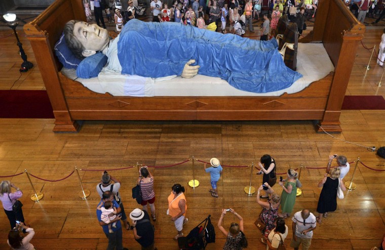 Image: Visitors look at a giant puppet of a grandmother sleeping on a bed in Liverpool