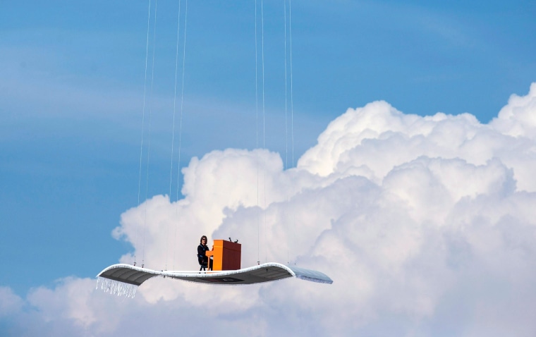 Image: German pianist Stefan Aaron plays an orange piano on a 'flying carpet' platform suspended from a helicopter, over the Munich airport