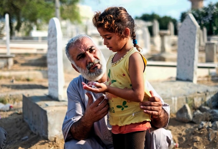 Image: A relative guides a girl in prayer at the grave of their loved one in a cemetery in Gaza city