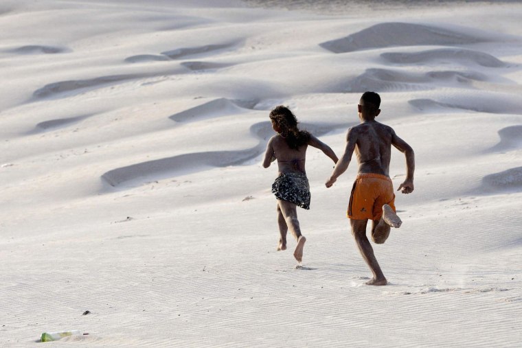 Image: Youths run along sand dunes during the peak of the summer vacation season on Atalaia beach in Salinopolis