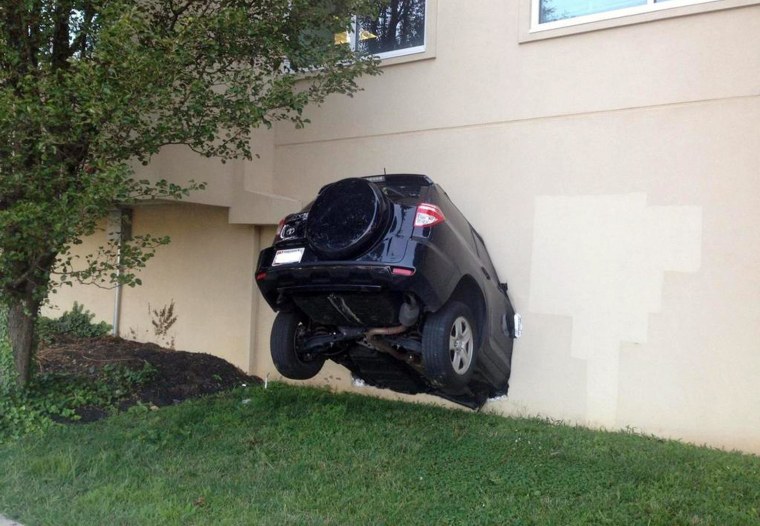 Image: An SUV hangs out of the side of a building that houses county offices after its driver drove into the building, injuring three people