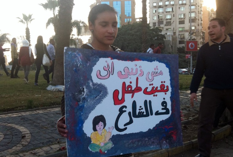 Image: A homeless girl holds a sign reading: "It is not my fault that I became a street child"