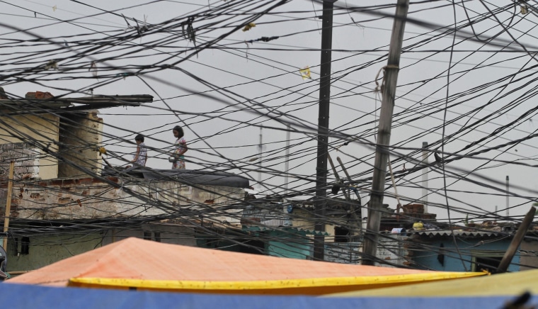 Image: Tangled overhead electric power cables are pictured at a residential area as children stand on the roof of a house in Noida