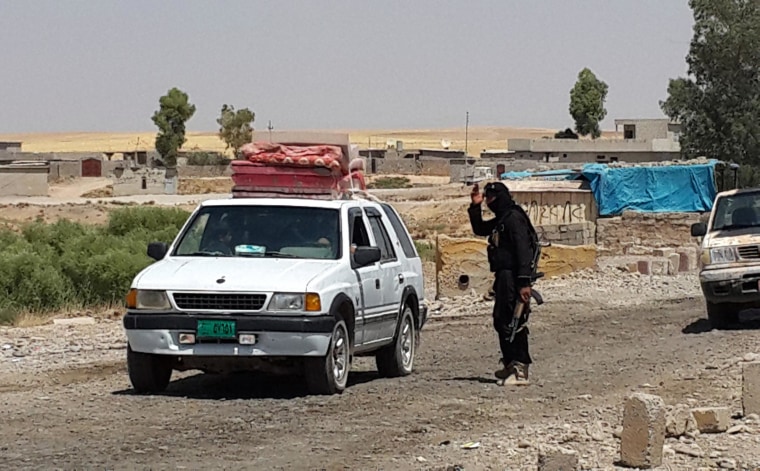 Image: A fighter with the Islamic State group directs a vehicle with a Christian family to leave from their home village outside Erbil