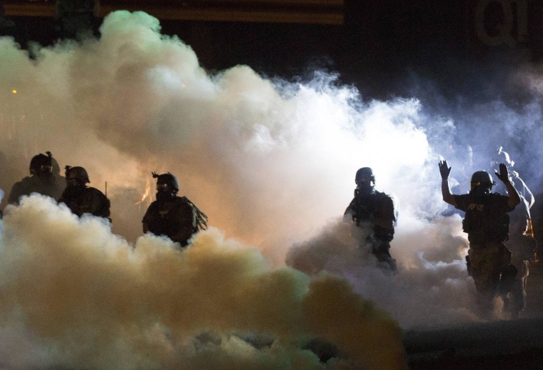 Riot police clear a street with smoke bombs while clashing with demonstrators in Ferguson, Missouri August 13, 2014. Police in Ferguson fired several rounds of tear gas to disperse protesters late on Wednesday, on the fourth night of demonstrations over the fatal shooting last weekend of an unarmed black teenager Michael Brown, 18, by a police officer on Saturday after what police said was a struggle with a gun in a police car. A witness in the case told local media that Brown had raised his arms to police to show that he was unarmed before being killed. REUTERS/Mario Anzuoni (UNITED STATES - Tags: CRIME LAW CIVIL UNREST)