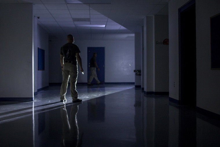 IMAGE: Shield Solutions instructor Jason Long stands at the end of a darkened hallway holding a knife, representing a school invader, while school employees practice their tactical maneuver
