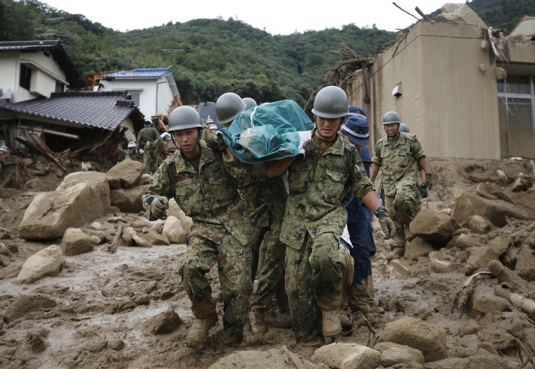 Image: JSDF soldiers and police officers carry the body of a victim in a plastic bag at a site where a landslide swept through a residential area at Asaminami ward in Hiroshima