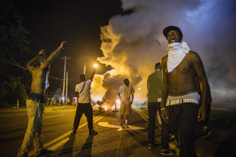 Image: Demonstrators stand in the middle of West Florissant as they react to tear gas fired by police during ongoing protests in reaction to the shooting of Michael Brown, in Ferguson