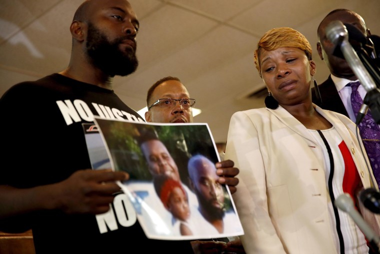 Lesley McSpadden, right, the mother of 18-year-old Michael Brown, watches as Brown's father, Michael Brown Sr., holds up a family picture of himself, his son, top left in photo, and a young child during a news conference Monday, Aug. 11, 2014, in Ferguson, Mo. Michael Brown, 18, was shot and killed in a confrontation with police in the St. Louis suburb of Ferguson, Mo,