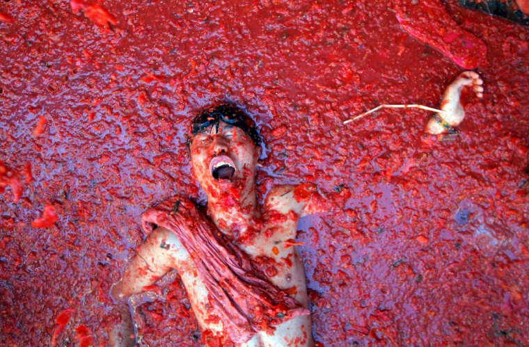 Image: A man lays in a puddle of squashed tomatoes, during the annual \"tomatina\" tomato fight fiesta in the village of Bunol
