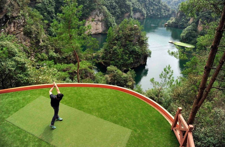 Image: Staff member plays a shot towards a putting green on a lake from a tee ground on top of a hill, at Zhangjiajie, Hunan province