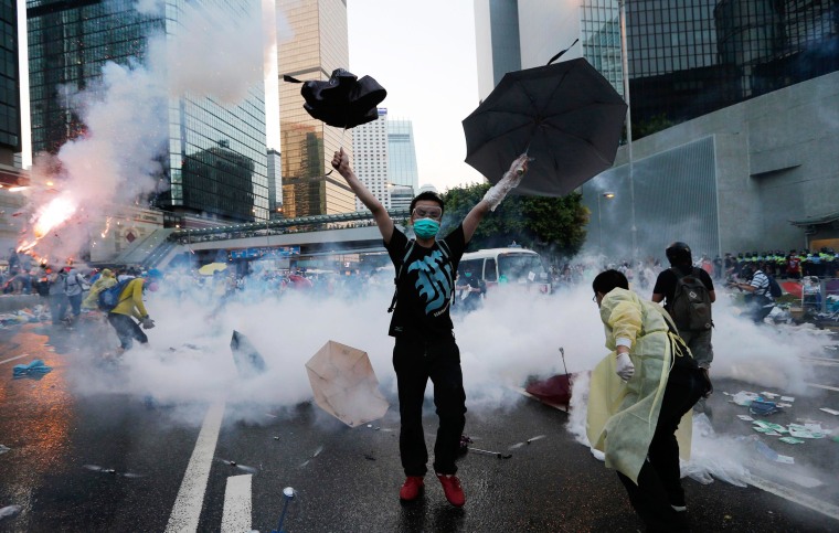 A protester raises his umbrellas near tear gas which was fired by riot police to disperse protesters blocking the main street to the financial Central district outside the government headquarters in Hong Kong.
