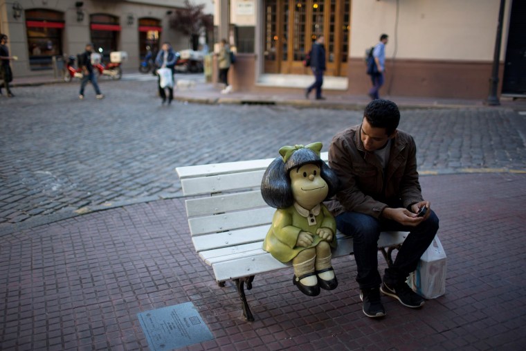 Image: A tourist sits on a bench beside the statue of comic strip characeter Mafalda