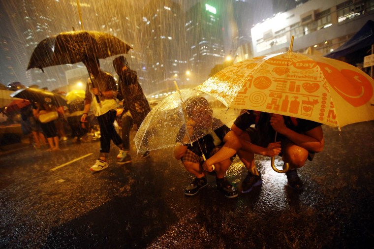 Image: Protesters take shelter from the rain under umbrellas as they block the main street to the financial Central district outside of the government headquarters in Hong Kong