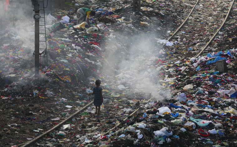 Image: A girl walks on a railway track past piles of dumped garbage in Mumbai, India