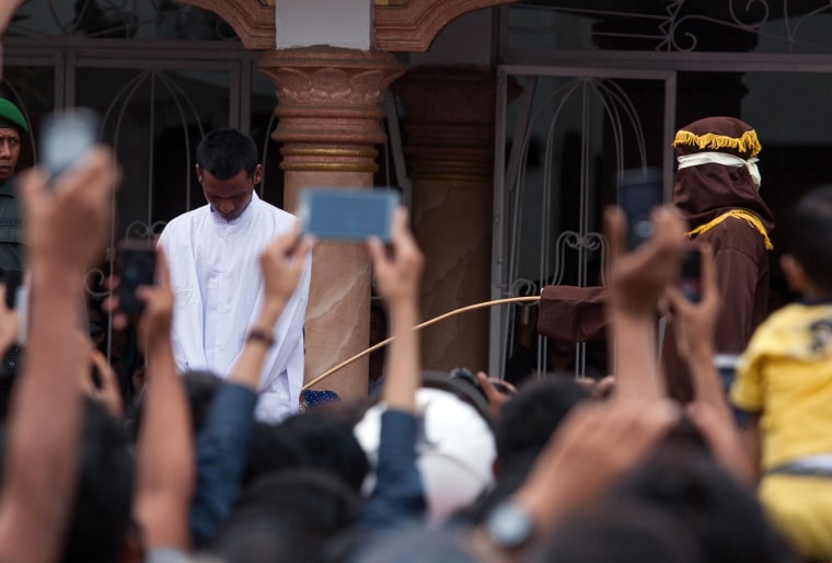 Image: A hooded official (right, wearing brown) caning a man in Banda Aceh