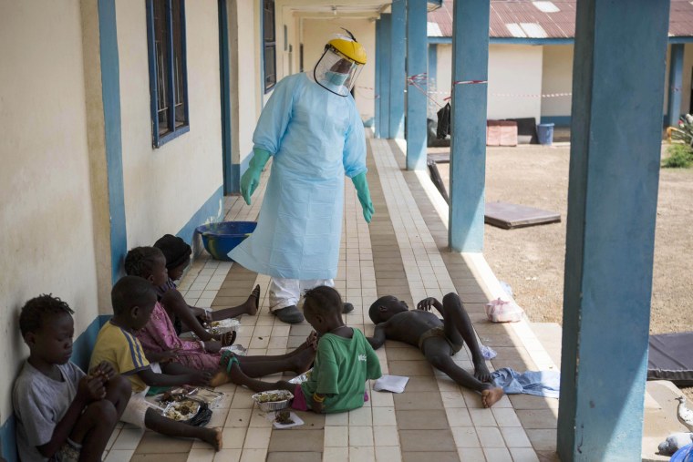 Image: A health official dressed in protective gear examines children suffering from the Ebola virus
