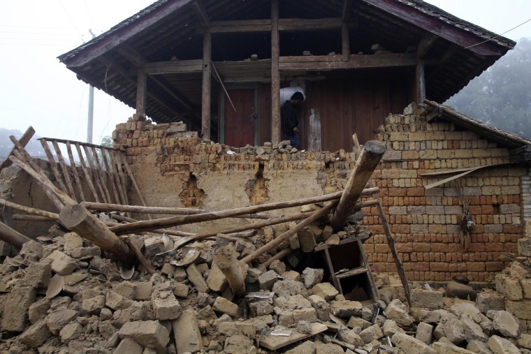 Image: A man carrying a bag walks past the ruins of a damaged house after an earthquake hit Yongping township of Jinggu county