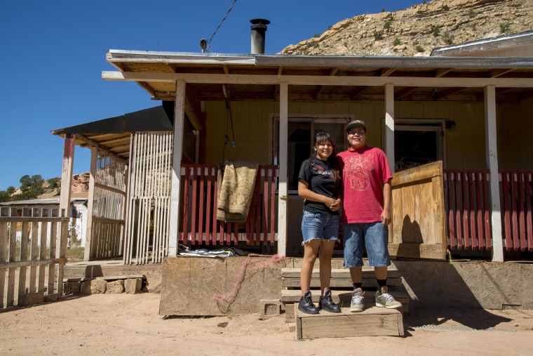 Image: The home of Tammy Lee sits below the mesa where she has lived her entire life. Her spouse Levi takes a picture with her on their front porch.