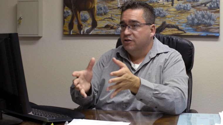 Image: Tim Delgado poses for a picture in front of the painting of galloping horses that hangs behind his desk in his office at Cash Cow.