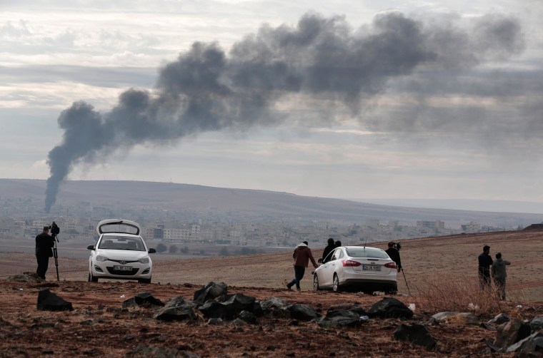 Image: Members of the media on a hilltop on the outskirts of Suruc, at the Turkey-Syria border, watch as smoke from a fire rises following a strike in Kobani, Syria