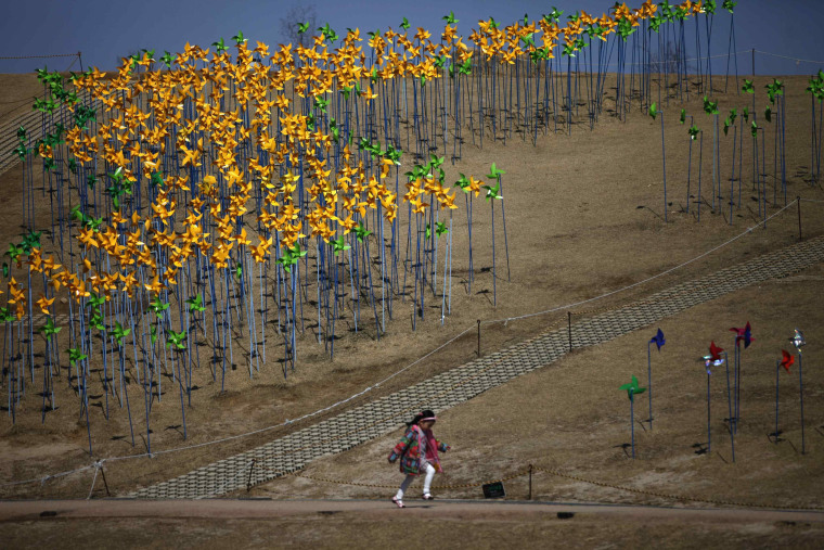 Image: A girl runs past pinwheels arranged in the shape of the Korean peninsula at Imjingak pavillion near the DMZ in Paju