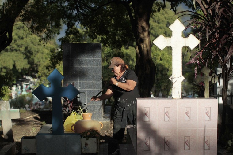 Image: Woman cleans the grave of a relative at a cemetery in the eve of All Saints Day in San Salvador