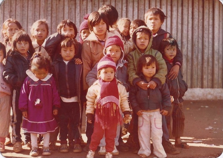 Monica Phromsavanh (front center) seen wearing a red hat and red scarf, with friends from the Laotian community inside a refugee camp in Argentina in 1986.