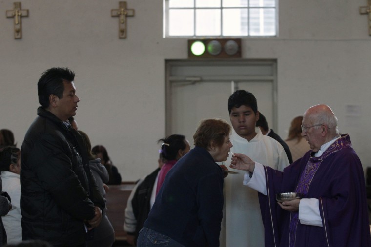 Image: A Catholic priest distributes Holy Communion to the congregation as a green light is lit inside St. Teresa of Avila church in Monterrey
