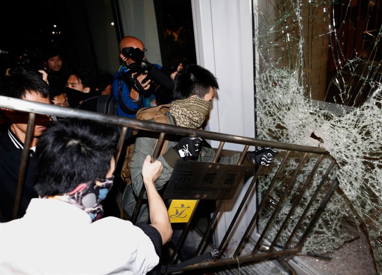Image: Masked pro-democracy protesters try to break  with a fence a glass window of the Legislative Council in Hong Kong