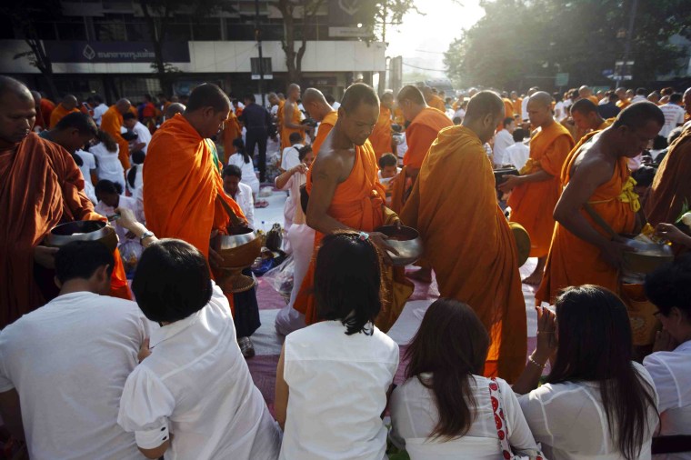 Image: Buddhist monks walk past people to collect donations from them during a mass alms-offering ceremony in Bangkok's shopping district
