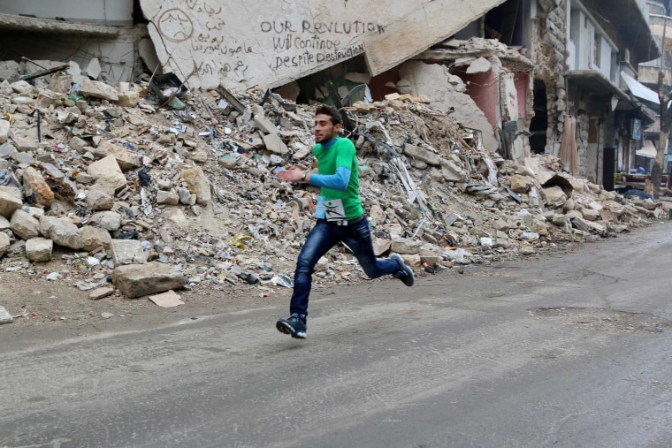 Image: A participant runs past a damaged building as he competes in a running race along a street in Aleppo's Bustan al-Qasr neighborhood