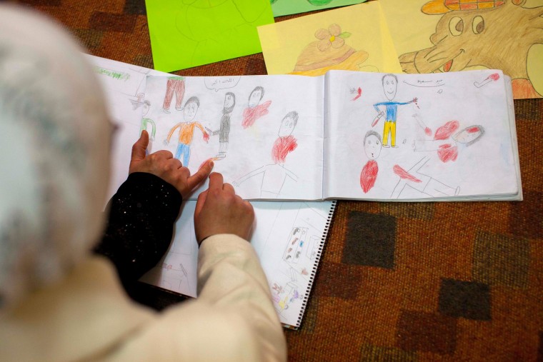 Image: Aya points at drawings, depicting violent scenes, she made recently, about life in Aleppo, Syria.