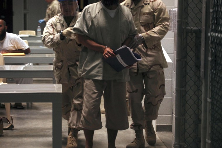 A Guantanamo detainee carries a workbook while escorted by guards who wear rubber gloves and face masks after attending a Life Skills class in the Camp 6 high-security detention facility on Guantanamo Bay U.S. Naval Base in Cuba. 
