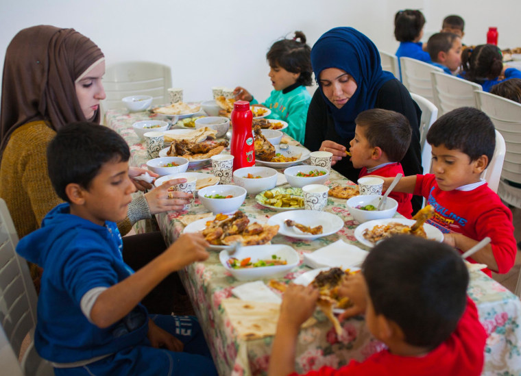 Siblings Obada, Amina, Hussein, Murad and Mustafa, sit at the lunch table with two staff members.