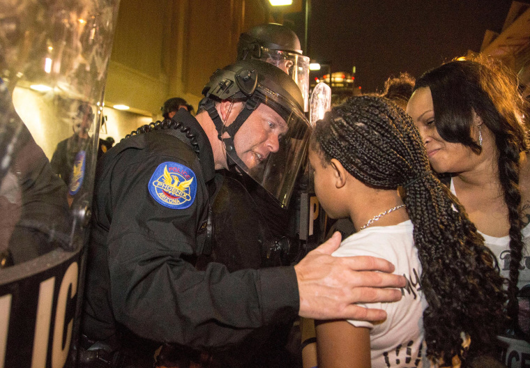 A Phoenix police officer in riot gear talks with Aiyana Rains, 9, the daughter of Rumain Brisbon, as she marches with hundreds of protesters toward police headquarters in Phoenix on Dec. 8, 2014. Grasping her hand, the officer said, "I'm sorry." 