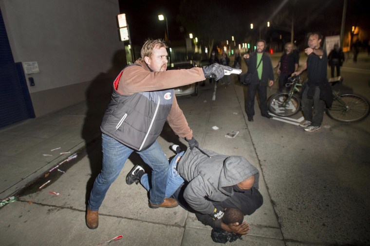 Image: An undercover police officer, who had been marching with anti-police demonstrators, aims his gun at protesters after some in the crowd attacked him and his partner in Oakland