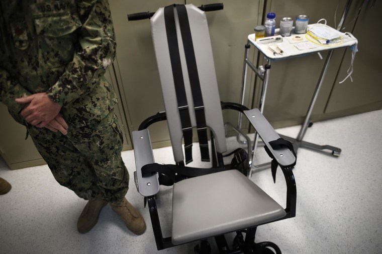 A U.S. Navy nurse stands next to a chair with restraints, used for force-feeding, and a tray displaying nutritional shakes, a tube for feeding through the nose, and lubricants, including a jar of olive oil, during a tour of the detainee hospital at Guantanamo Bay Naval Base in Cuba.