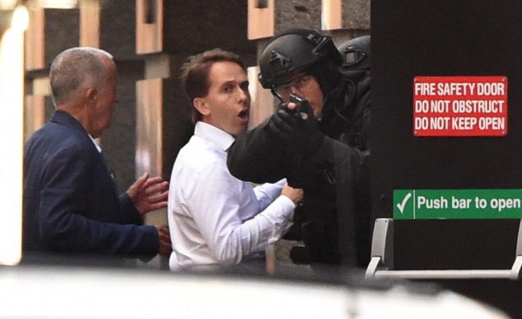 Two hostages run for cover behind a policeman during a hostage siege in the central business district of Sydney on December 15, 2014.  Three people ran out of a Sydney cafe where a gunman has taken hostages and displayed an Islamic flag against the window, police said December 15, adding that no one has yet been harmed. 