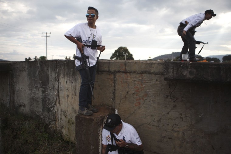 Image: Vigilantes stand guard next to a bridge during a blockade on a highway near the town of Uruapan in Michoacan state